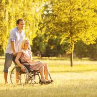 Portrait of an young couple, man and disabled woman in wheelchair walking in a park.